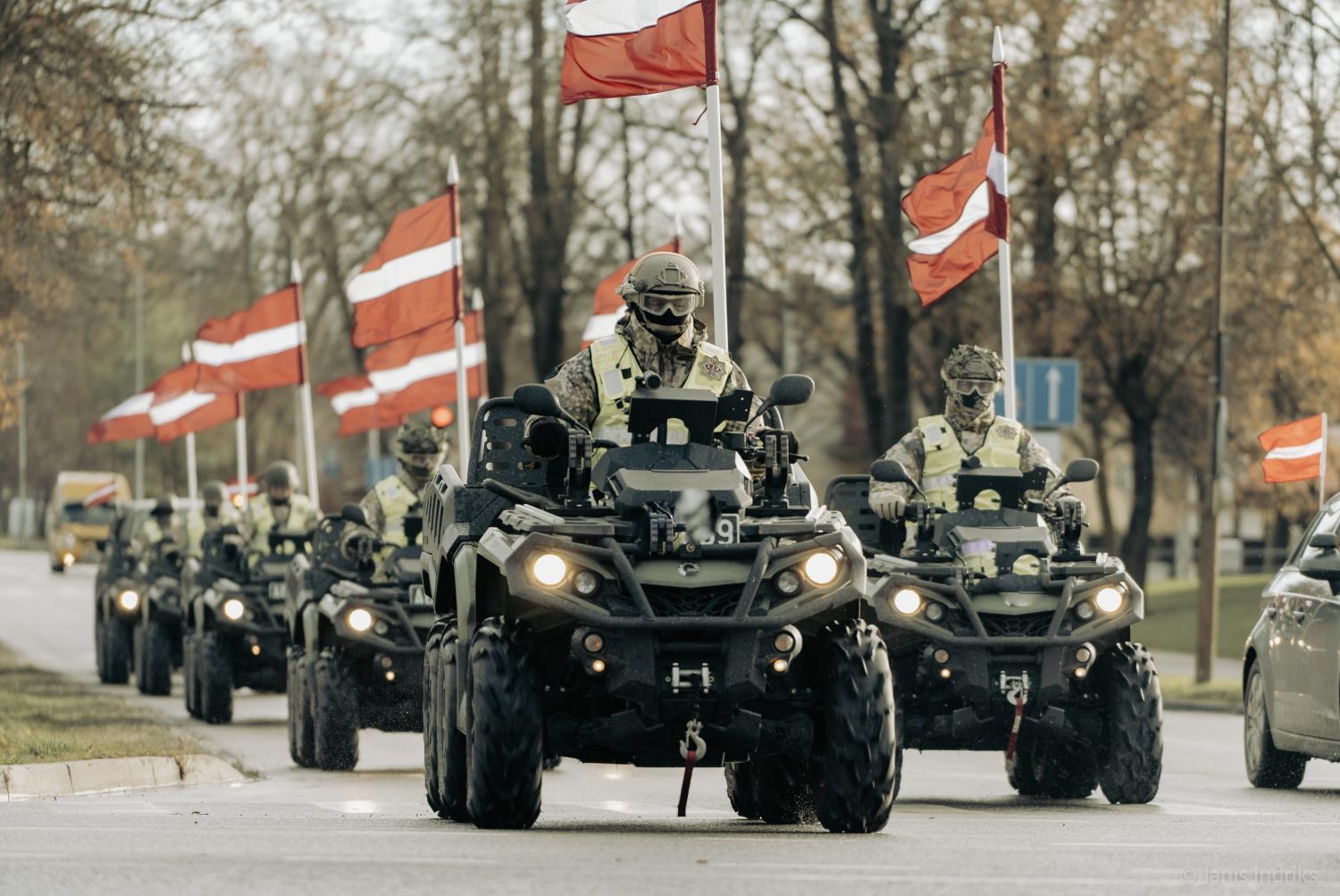 Seši ar Latvijas karogiem izrotāti sešriteņu kvadricikli “Bombardier 650”, uz kuriem sēž zemessargi kaujas ekipējumā dodas militārajā maršā cauri pilsētai.