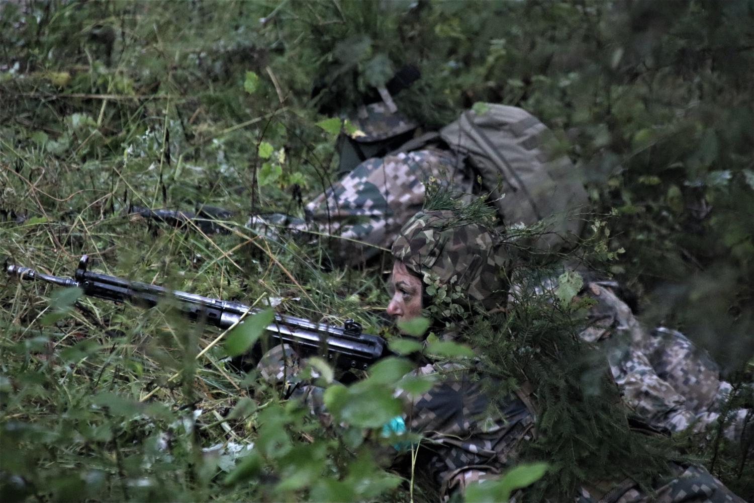 Divi zemessargi ar ieročiem guļ pozīcijās meža biezoknī un novēro sektoru