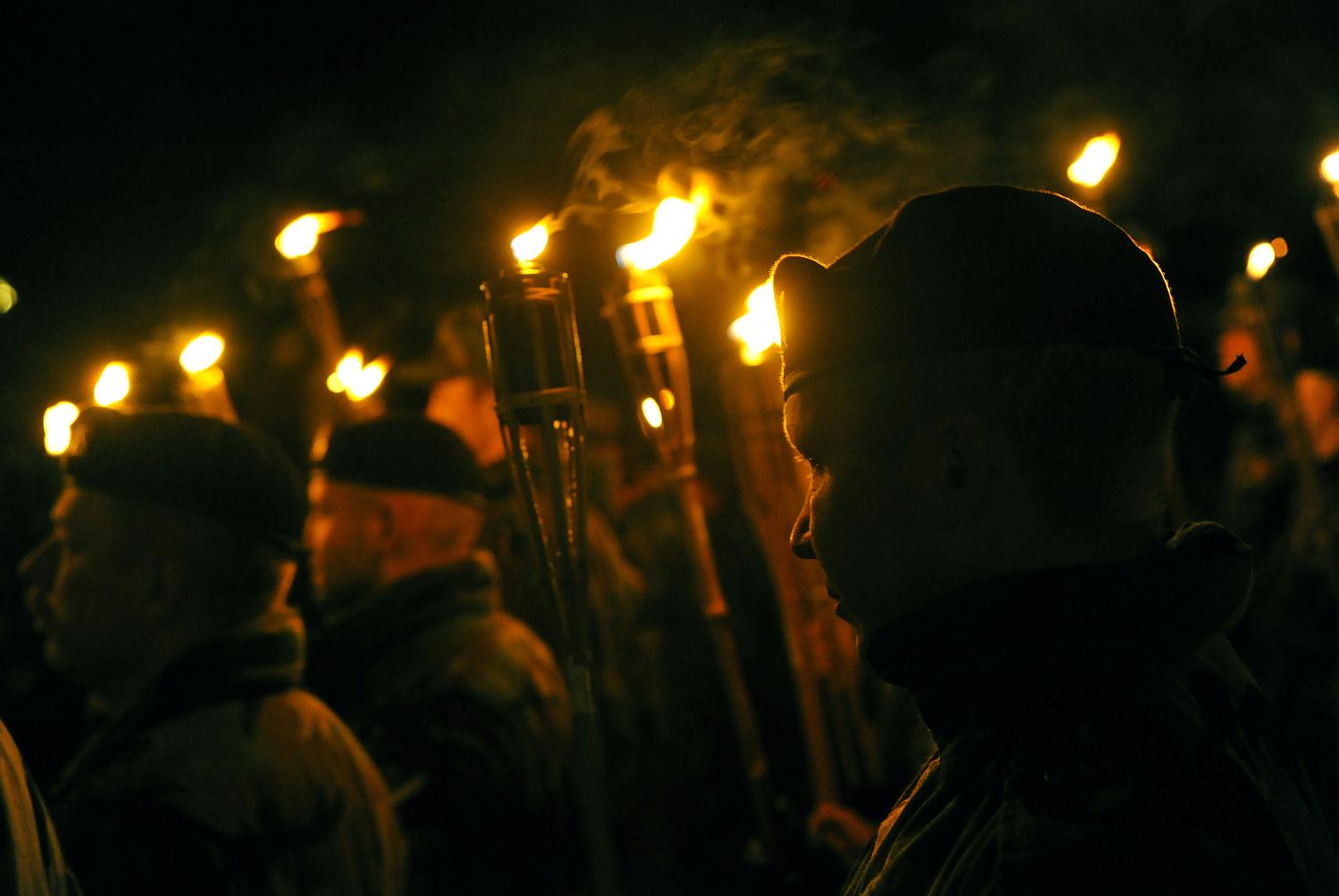 Zemessargi formas tērpos un beretēs tumsā iet lāpu gājienā