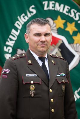 Pulkvežleitnanta Rinata Ažēna portrets svētku formastērpā uz Zemessardzes 45. kaujas nodrošinājuma bataljona karoga fona