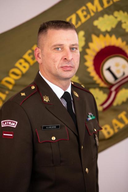 Majora Aivja Vācera portrets svētku formastērpā uz Zemessardzes 51. kājnieku bataljona karoga fona